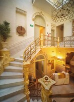 A grand staircase with ornate railings and a chandelier, leading to a second-floor area with a reception desk and a door marked 'Exit.'