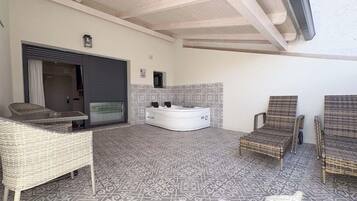 Una habitación con un ventanal grande, una bañera blanca y una zona de estar con mobiliario de mimbre.