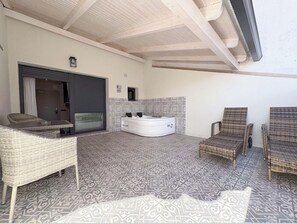 Una habitación con un ventanal grande, una bañera blanca y una zona de estar con mobiliario de mimbre.