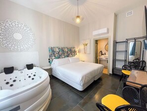Habitación de hotel con una bañera grande, una cama, un rincón de comedor con sillas y una pared decorativa.
