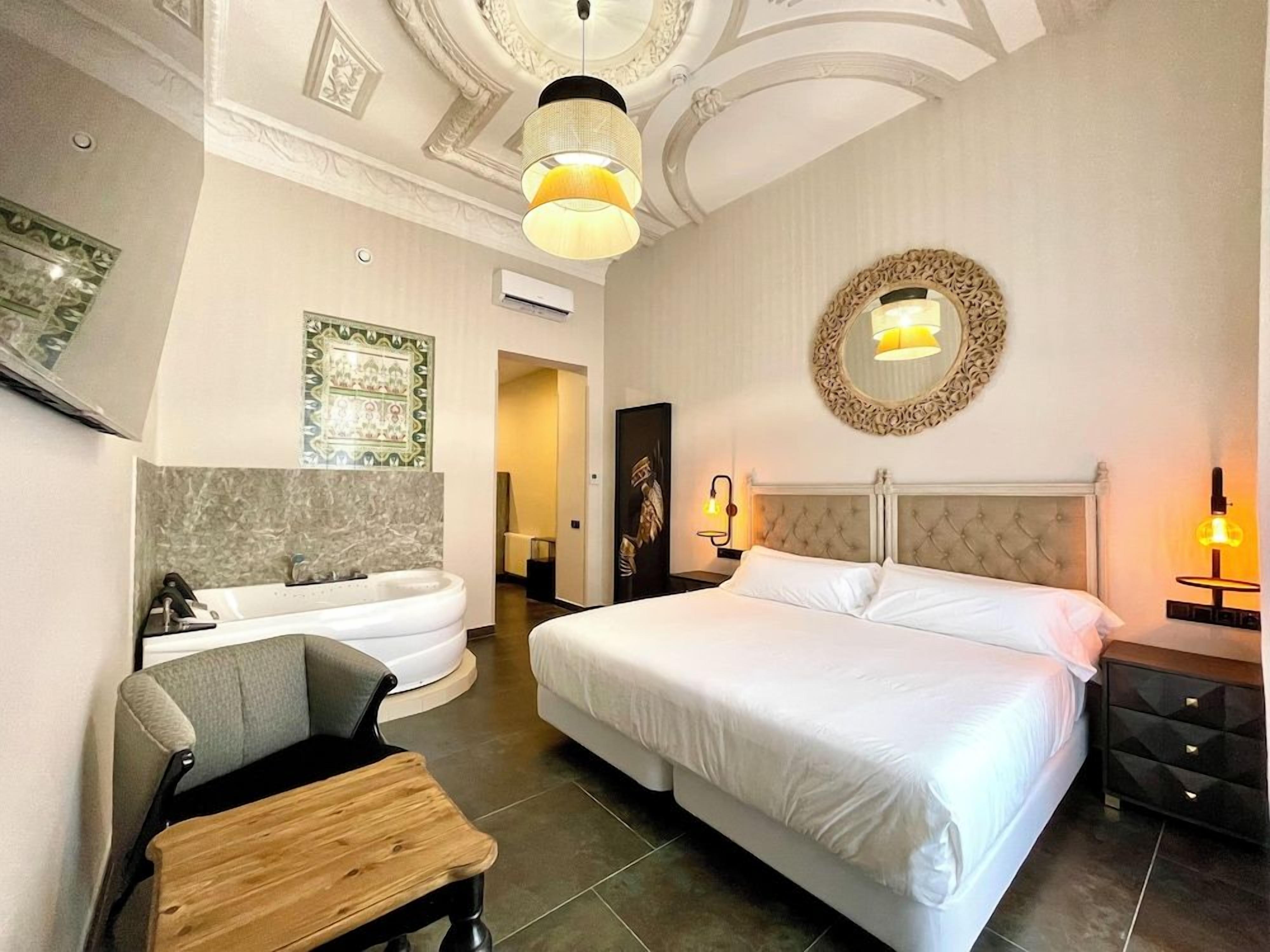 Habitación de hotel con una cama grande, una zona de estar, una bañera y un espejo en la pared.