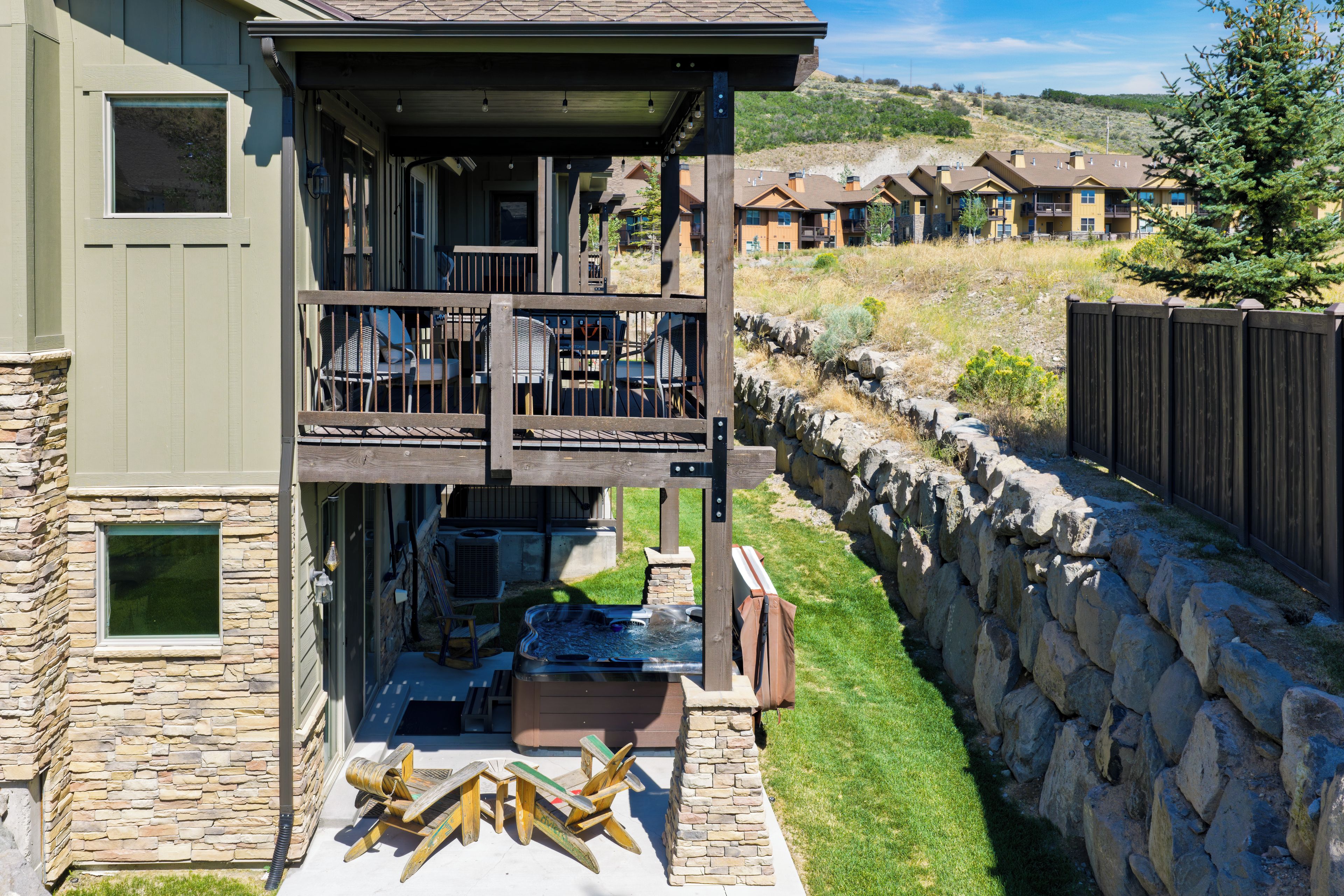 A two-story building with a covered outdoor seating area, stone walls, and a view of other buildings in the background.