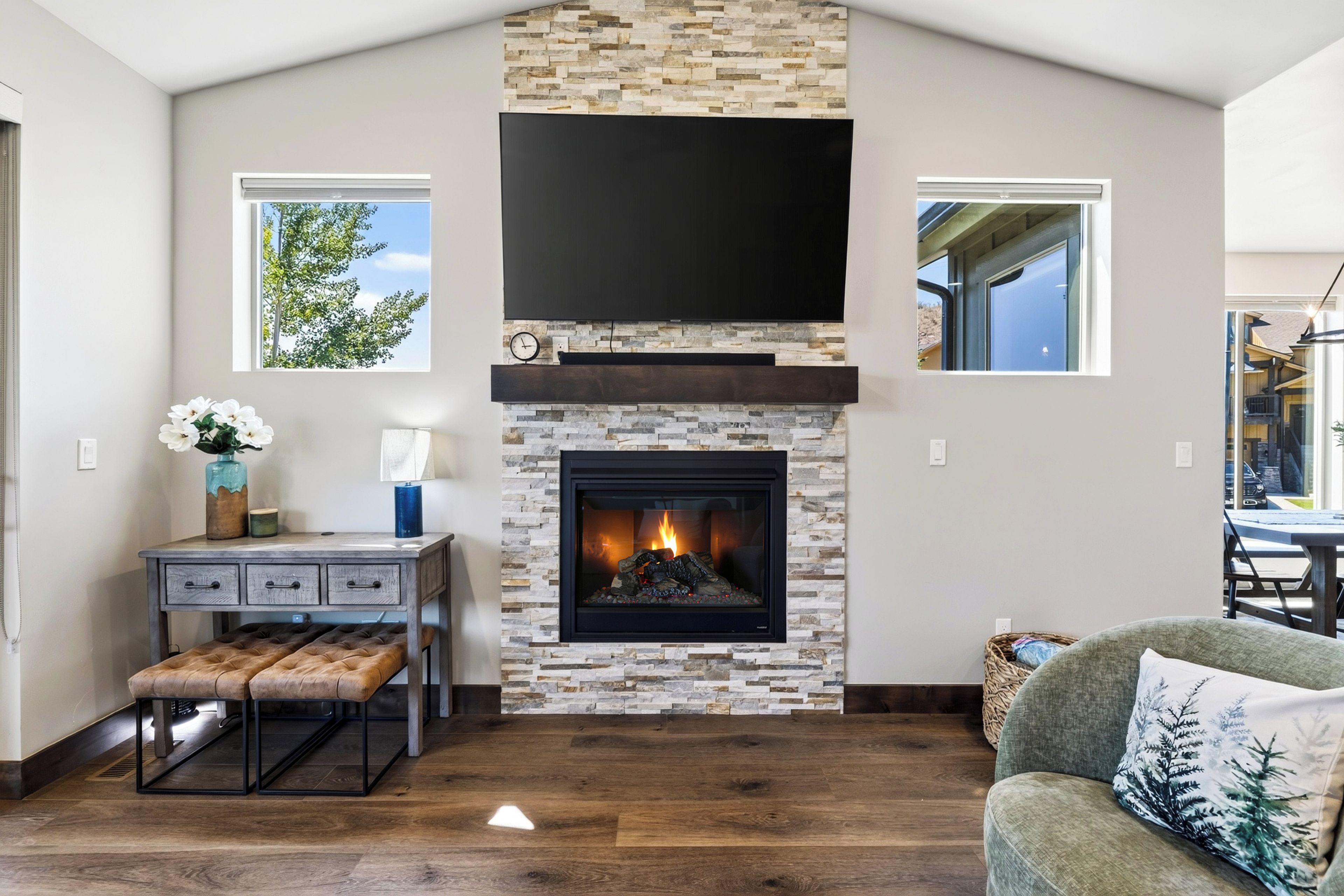 A living room with a stone fireplace, a flat-screen TV mounted above it, and a window on the left wall.