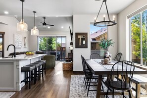 Een moderne keuken met een centraal eiland, barkrukken en een eethoek met een grote tafel en stoelen.