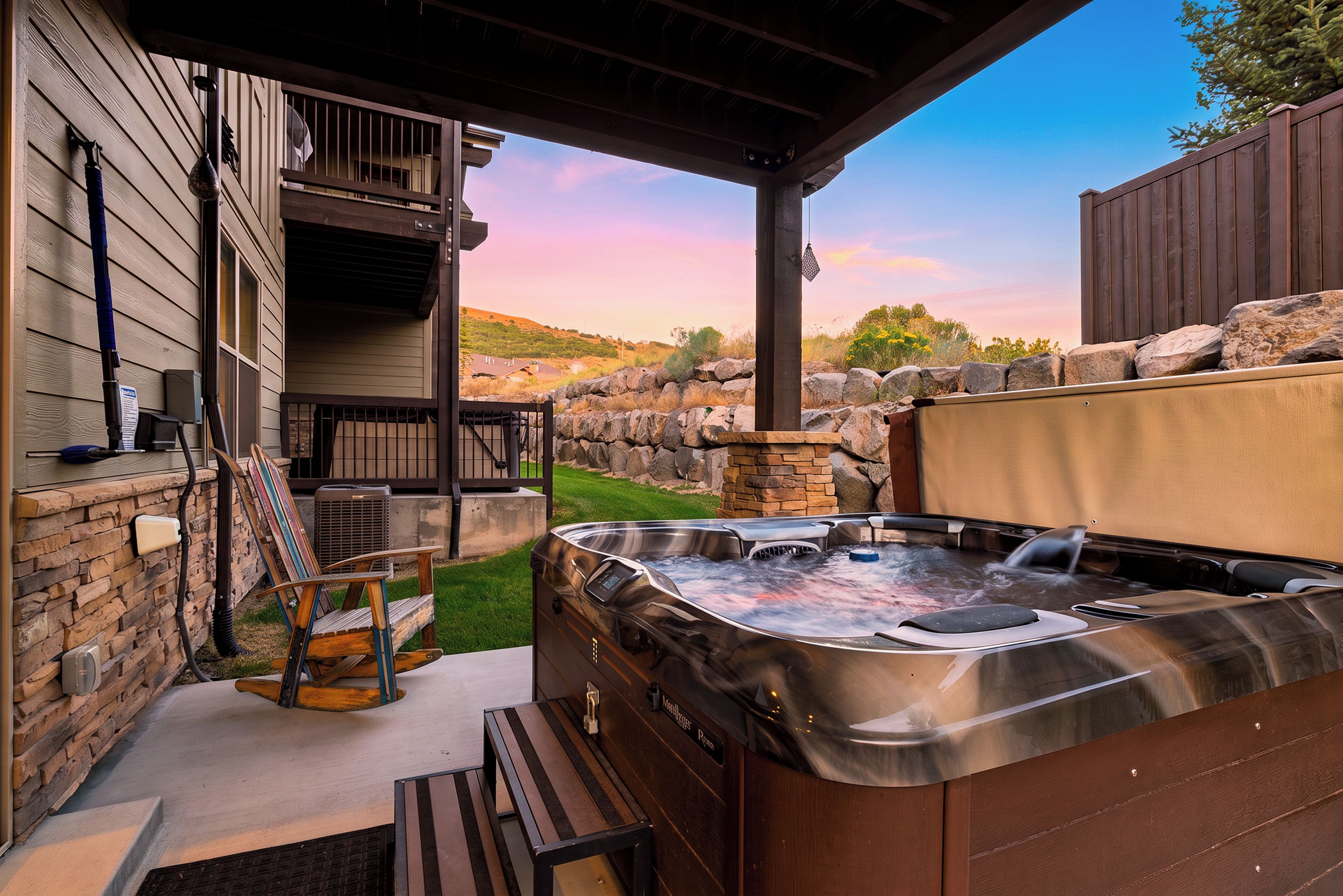 Un jacuzzi en un entorno exterior con pared de piedra, terraza de madera y zona cubierta.