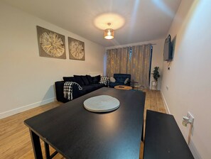 A modern living room with a dark wooden table, a black sofa, and two wall-mounted abstract art pieces. - Cozy Nest North Farm Rd Tunbridge Wells (Royal Tunbridge Wells)