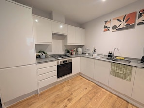 A modern kitchen with white cabinetry, a gas stove, an oven, and a sink. - Cozy Nest North Farm Rd Tunbridge Wells (Royal Tunbridge Wells)