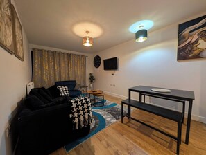 A modern living room with a sofa, a coffee table, a TV, and a painting on the wall. - Cozy Nest North Farm Rd Tunbridge Wells (Royal Tunbridge Wells)