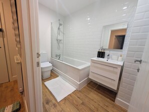 Et moderne badeværelse med et glasafskærmet brusebad, et hvidt toilet, en vask med spejl og en trægulv.