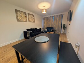 A modern living room with a dark wooden dining table, a black sofa, and two wall-mounted paintings. - Cozy Nest North Farm Rd Tunbridge Wells (Royal Tunbridge Wells)