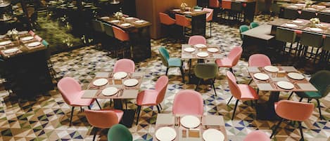 A restaurant with multiple tables set for dining, featuring geometric patterned flooring and a variety of chair colors.