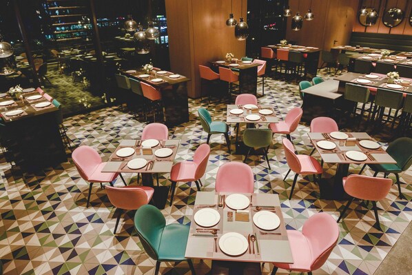 A restaurant with multiple tables set for dining, featuring geometric patterned flooring and a variety of chair colors.