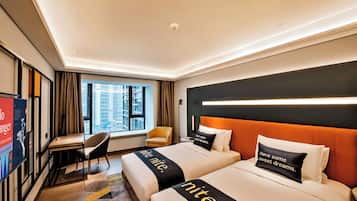 Quarto de hotel com duas camas, uma escrivaninha, uma cadeira, janela com vista para a cidade e um aviso na parede.