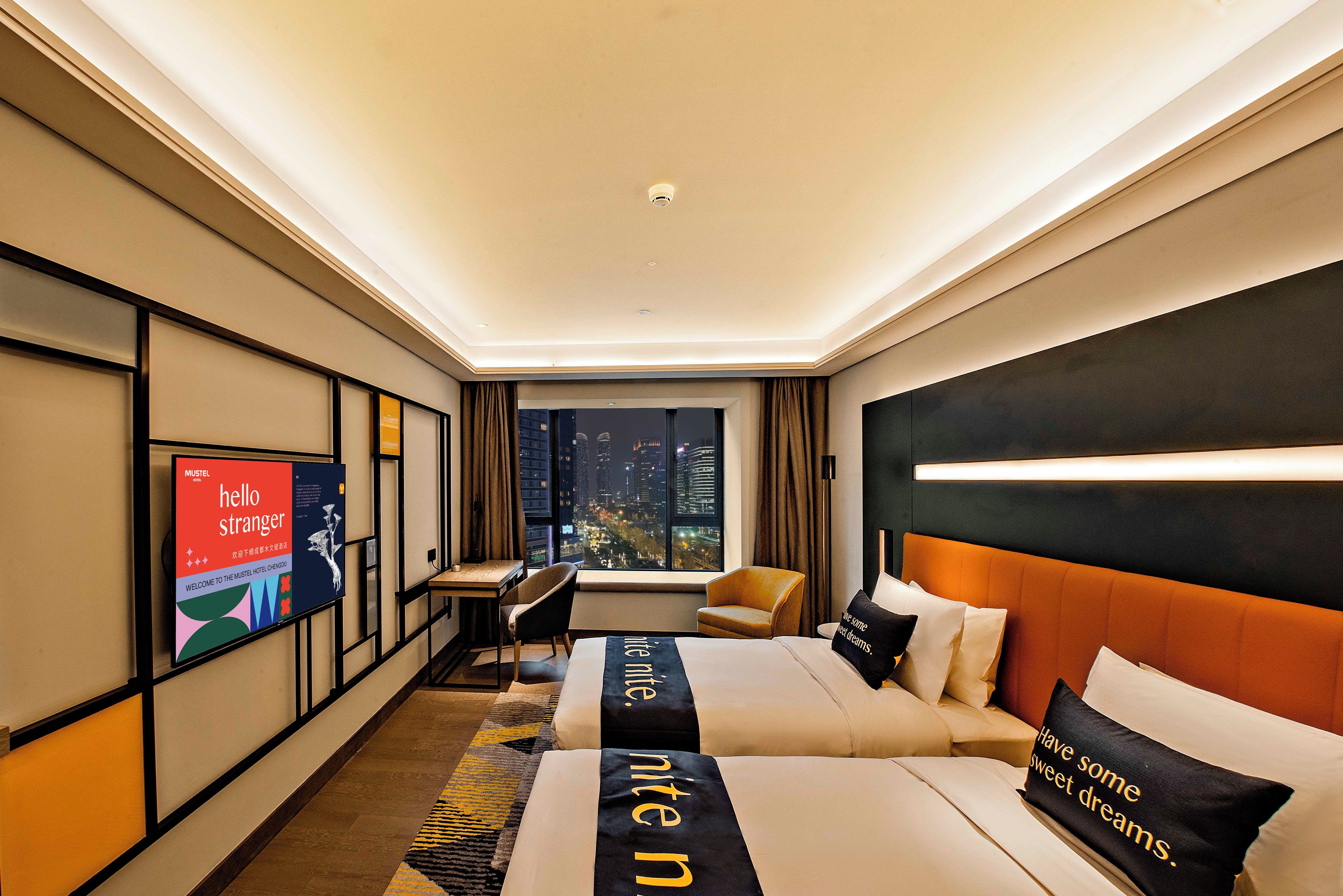 A modern hotel room with a city view, a desk, a chair, a bed with a headboard, and a television on the wall.