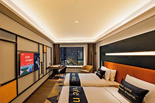 A modern hotel room with a city view, a desk, a chair, a bed with a headboard, and a television on the wall.