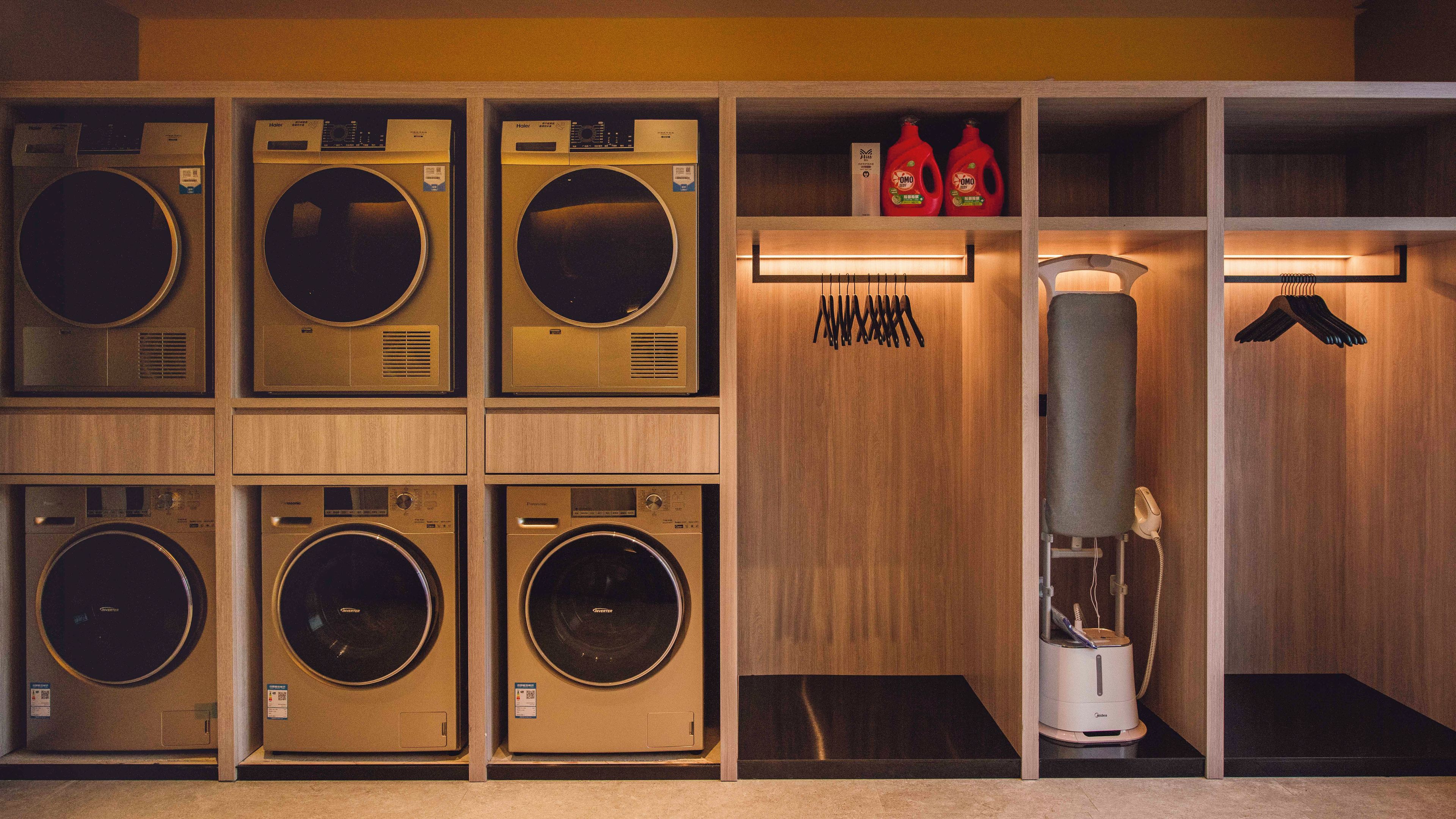 A laundry facility with multiple washing machines and dryers, a water heater, and a set of iron and ironing board.