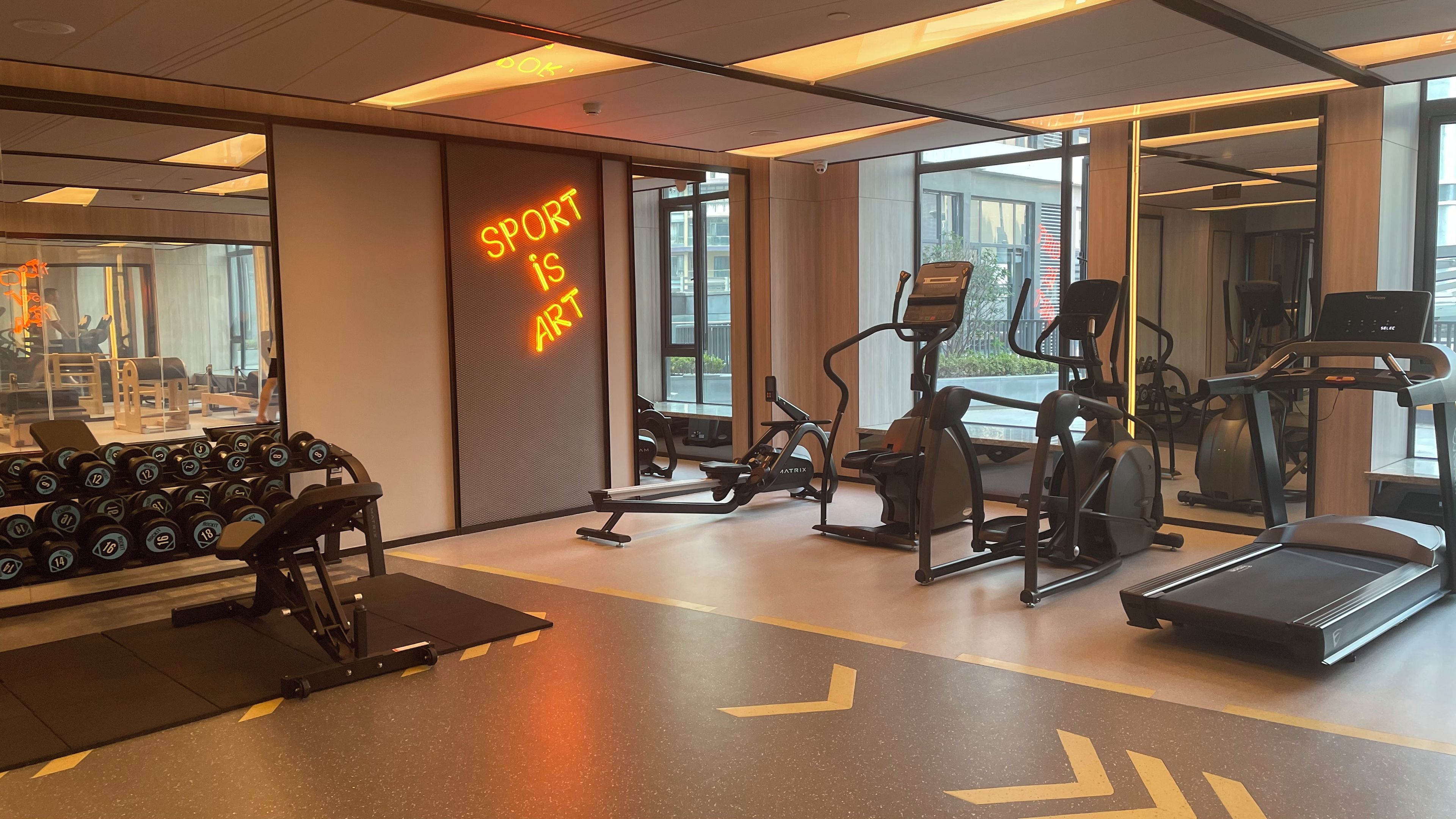 A gym with exercise equipment, a mirror, and a neon sign stating 'SPORT is ART'.