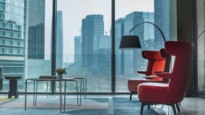 Una sala de estar moderna con una butaca roja, una lámpara de pie negra y vistas a un paisaje urbano a través de amplios ventanales.