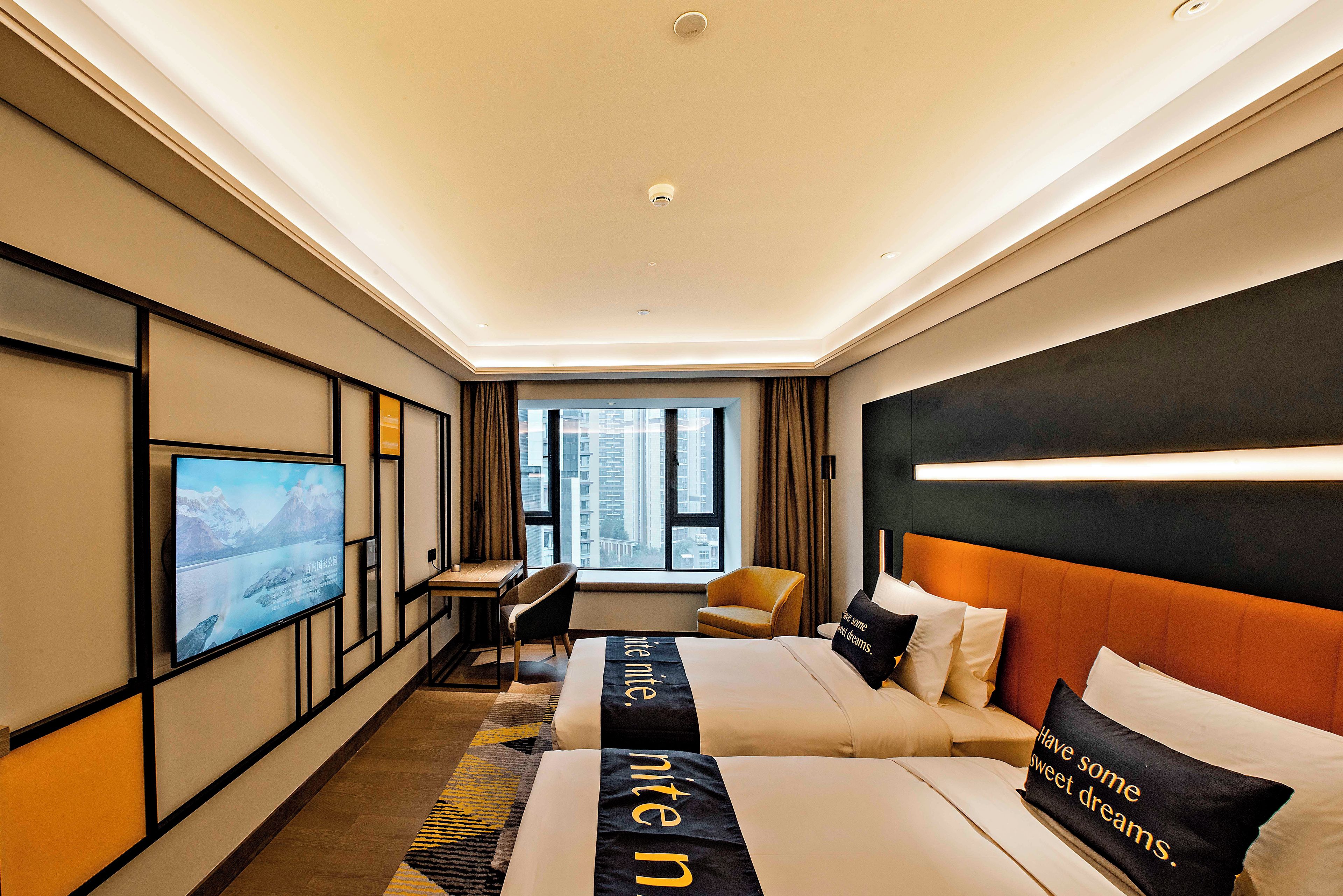 A hotel room with a bed, a desk, a chair, a TV, and a view of the city.