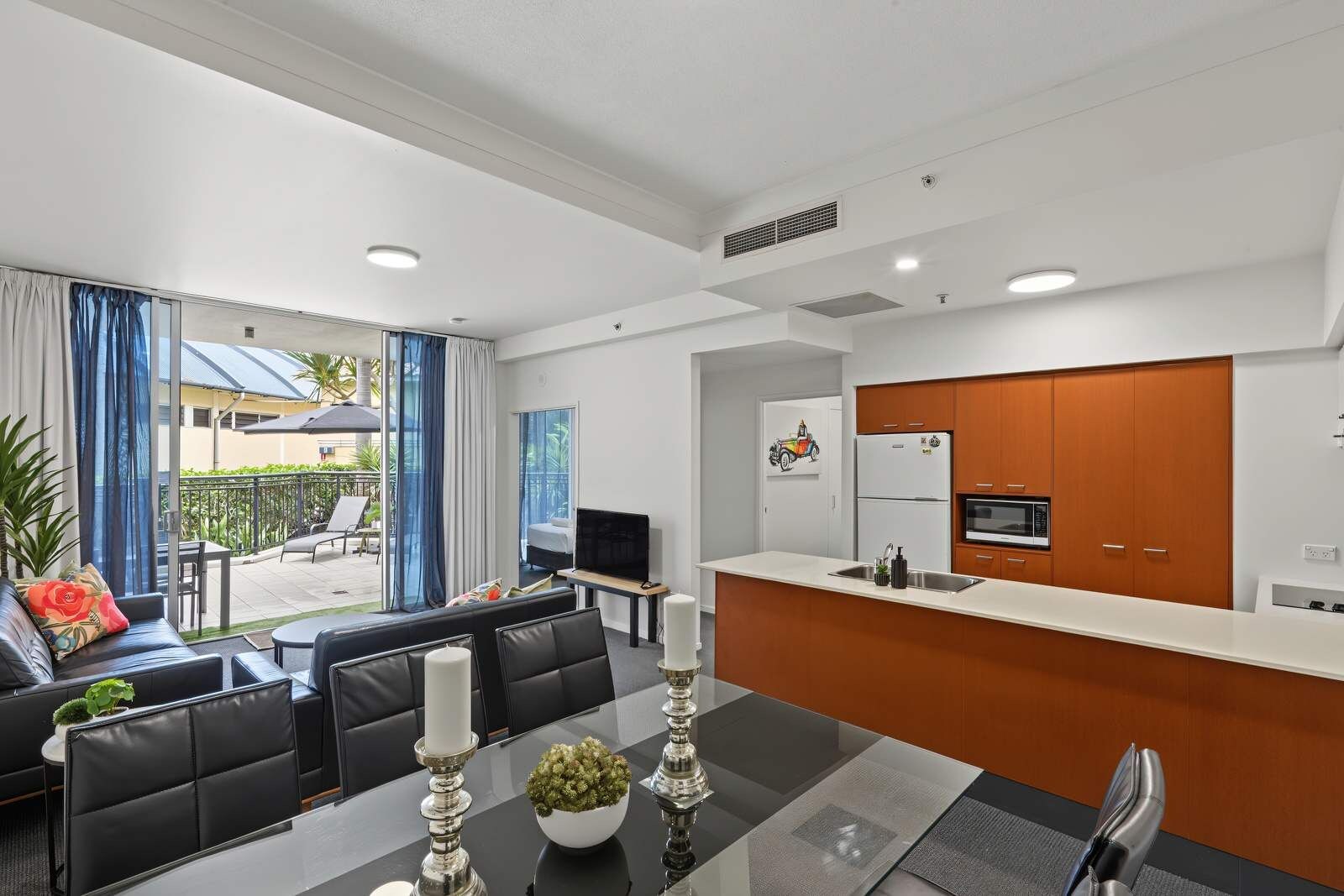 A modern hotel room with a dining area, a kitchen, and a balcony with outdoor furniture.