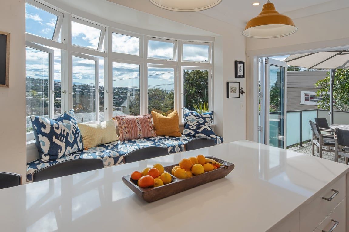 A modern kitchen with a large window, a built-in bench, and a fruit bowl on the counter.