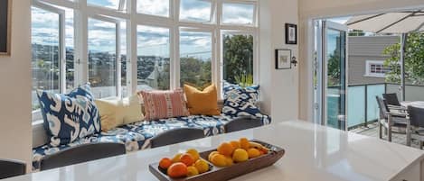 A modern kitchen with a large window, a built-in bench, and a fruit bowl on the counter.