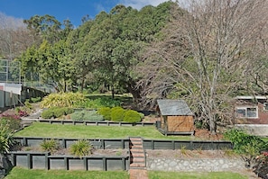 A landscaped garden with a wooden structure, stone walls, and various plants. - Sunset Paradise - Views, Hot Tub & Walk to Town (Nelson South)