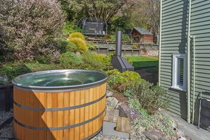 A wooden hot tub in a garden with a wooden deck, a wooden cabin, and a cable car in the background. - Sunset Paradise - Views, Hot Tub & Walk to Town (Nelson South)