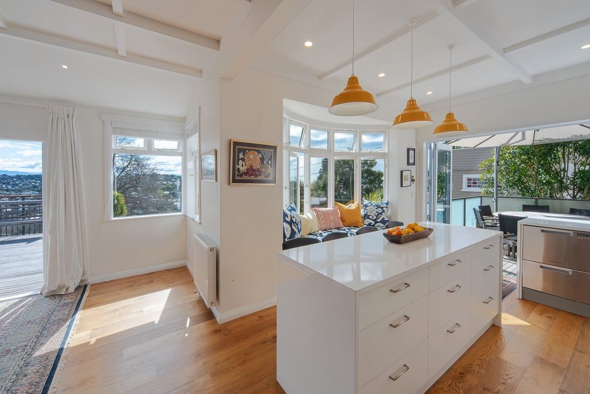 Une cuisine moderne dotée d’un îlot central, de luminaires suspendus et offrant une vue sur l’extérieur.