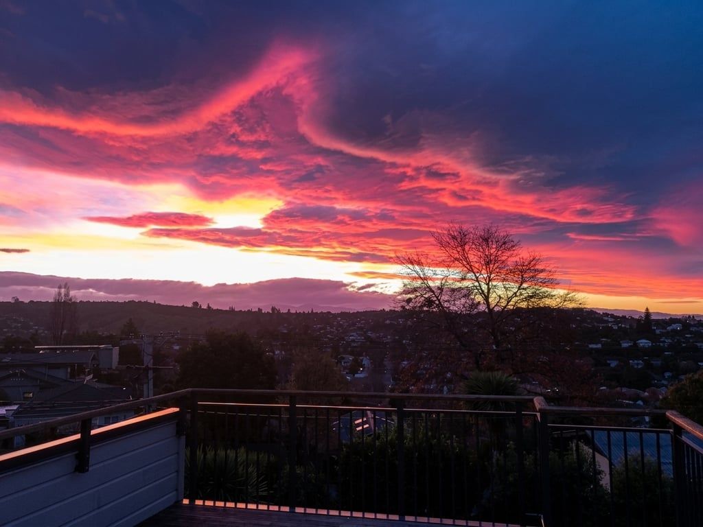Une vue sur le coucher de soleil depuis un balcon doté d’une balustrade, donnant sur un quartier résidentiel.