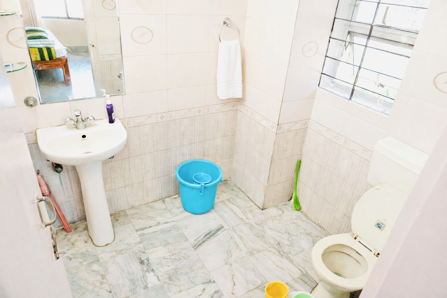 A bathroom with a sink, toilet, and a blue bucket.