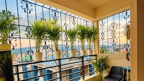 A balcony with a railing, potted plants, a small table, and a chair. - Rooftop Cityscape Inn || Luxurious 3BHK Apartment || Cityview (Guwahati)