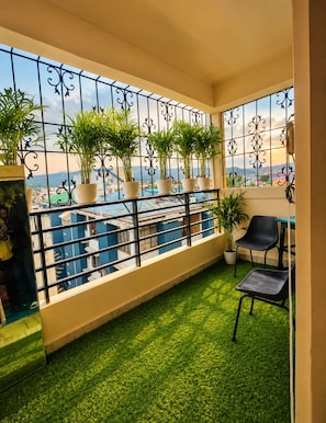 A balcony with a railing, potted plants, a small table, and a chair. - Rooftop Cityscape Inn || Luxurious 3BHK Apartment || Cityview (Guwahati)