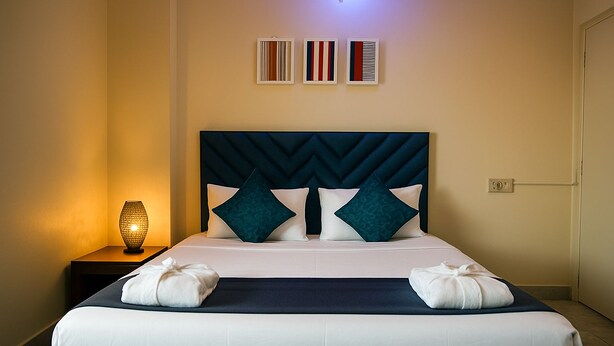 A neatly made bed with a headboard, two pillows, and a bedside lamp. - Rooftop Cityscape Inn || Luxurious 3BHK Apartment || Cityview (Guwahati)