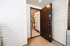 A hallway with a white brick wall, a wooden door, and a tiled floor. - Nikyo Yume DreamCat Villa Osaka (Osaka)