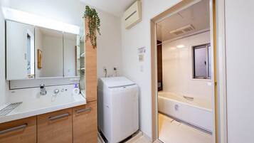 A compact hotel room with a kitchenette, a washing machine, and a shower area.