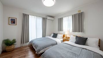 A hotel room with two beds, a bedside table with a lamp, a potted plant, and a framed picture on the wall.