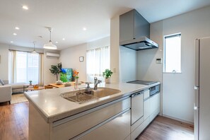 A modern kitchen with a central island, stainless steel appliances, and a large window providing natural light. - Nikyo Yume DreamCat Villa Osaka (Osaka)