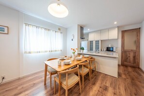 A modern kitchen with white cabinets, a wooden dining table, and a built-in microwave. - Nikyo Yume DreamCat Villa Osaka (Osaka)