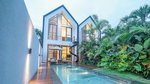 Una casa moderna con piscina, rodeada de exuberante vegetación.