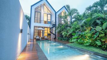 A modern house with a pool, surrounded by lush greenery.
