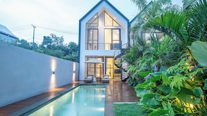 Una casa moderna con piscina, un espacio de estar techado al aire libre y abundante vegetación.