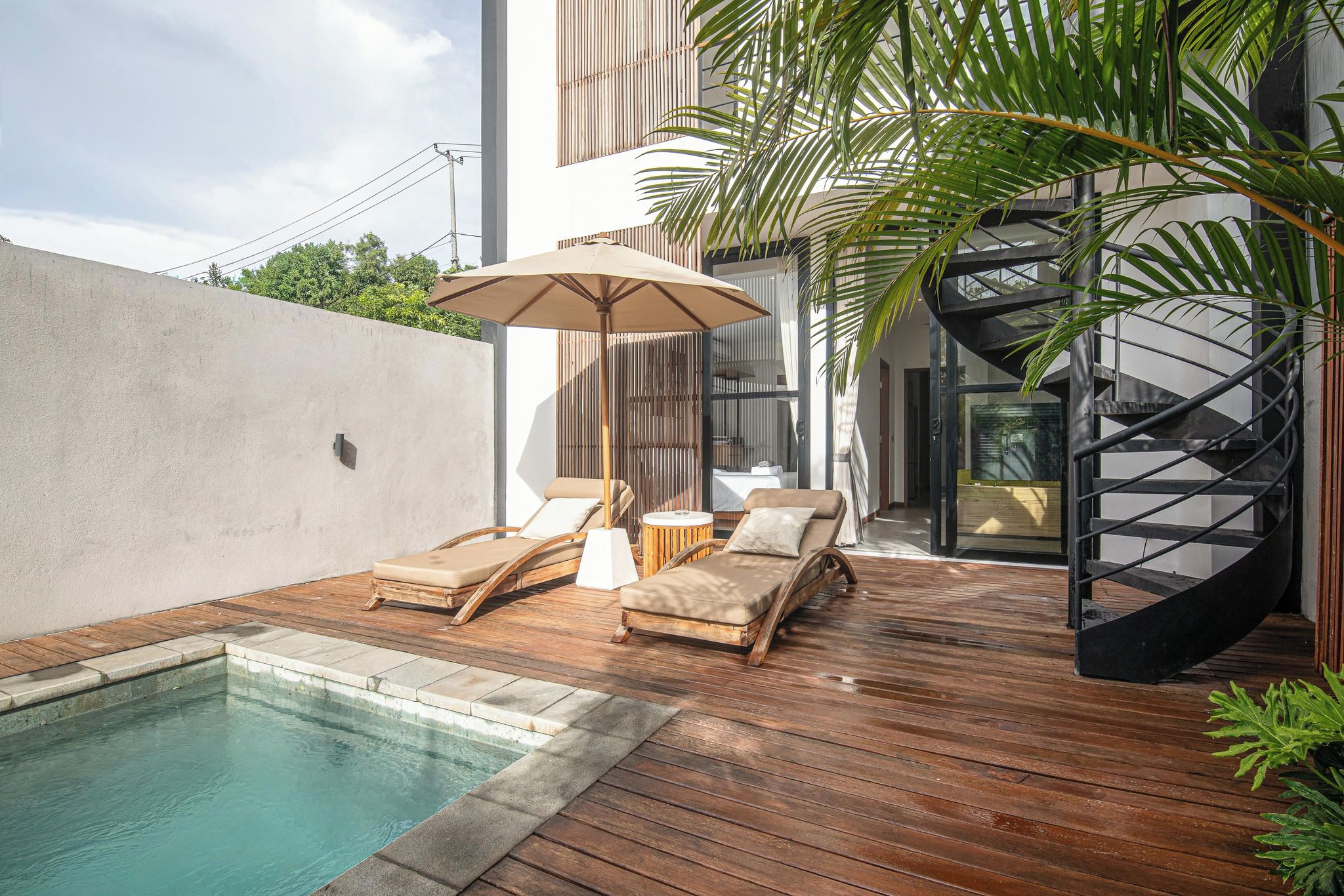 A poolside area with wooden decking, lounge chairs, and a spiral staircase.