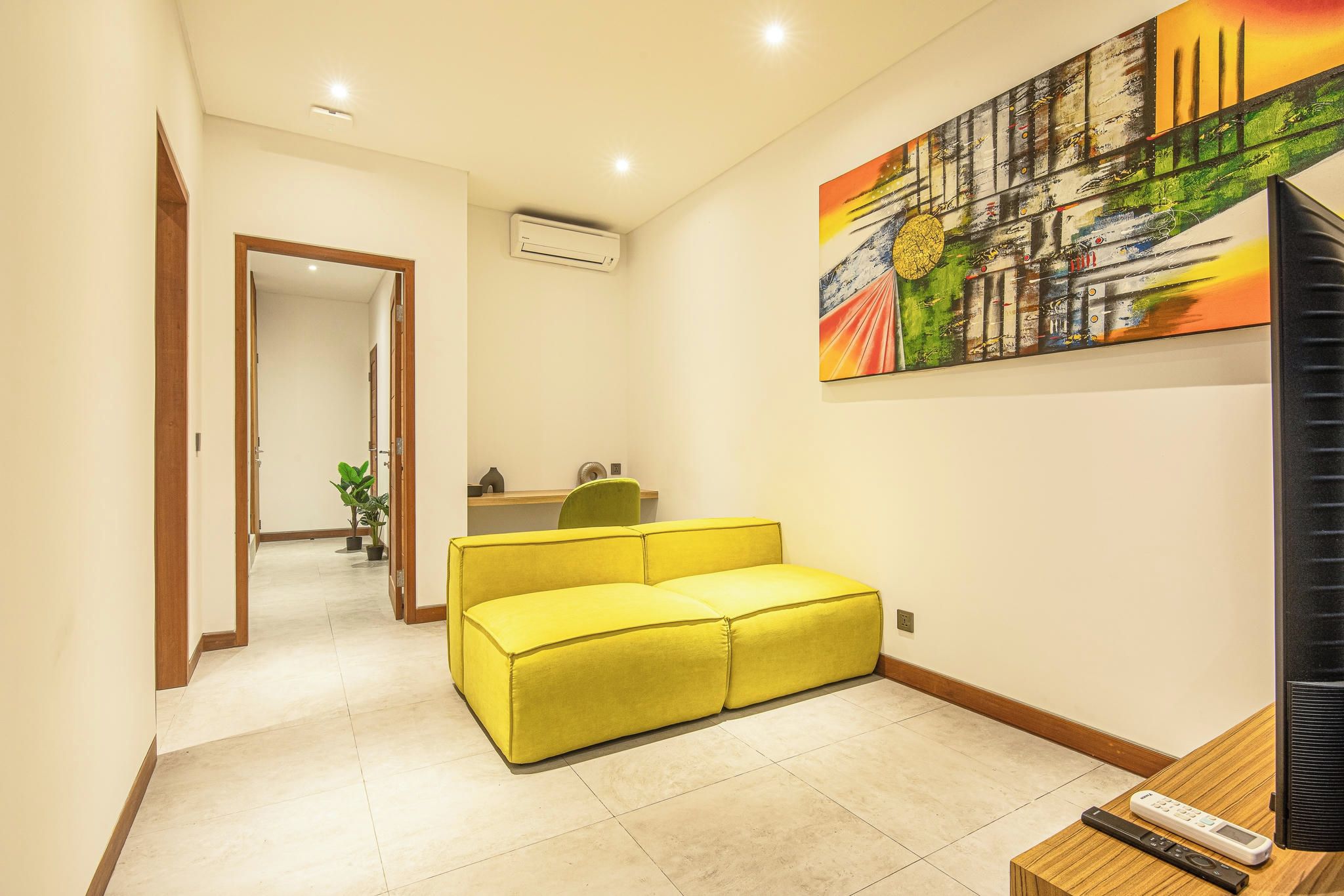 Un pasillo con un sofá amarillo, un cuadro en la pared y un televisor sobre una mesa de madera.