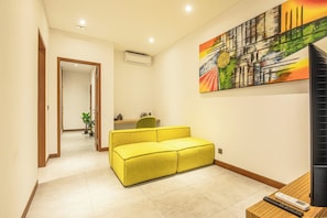 Un pasillo con un sofá amarillo, un cuadro en la pared y un televisor sobre una mesa de madera.
