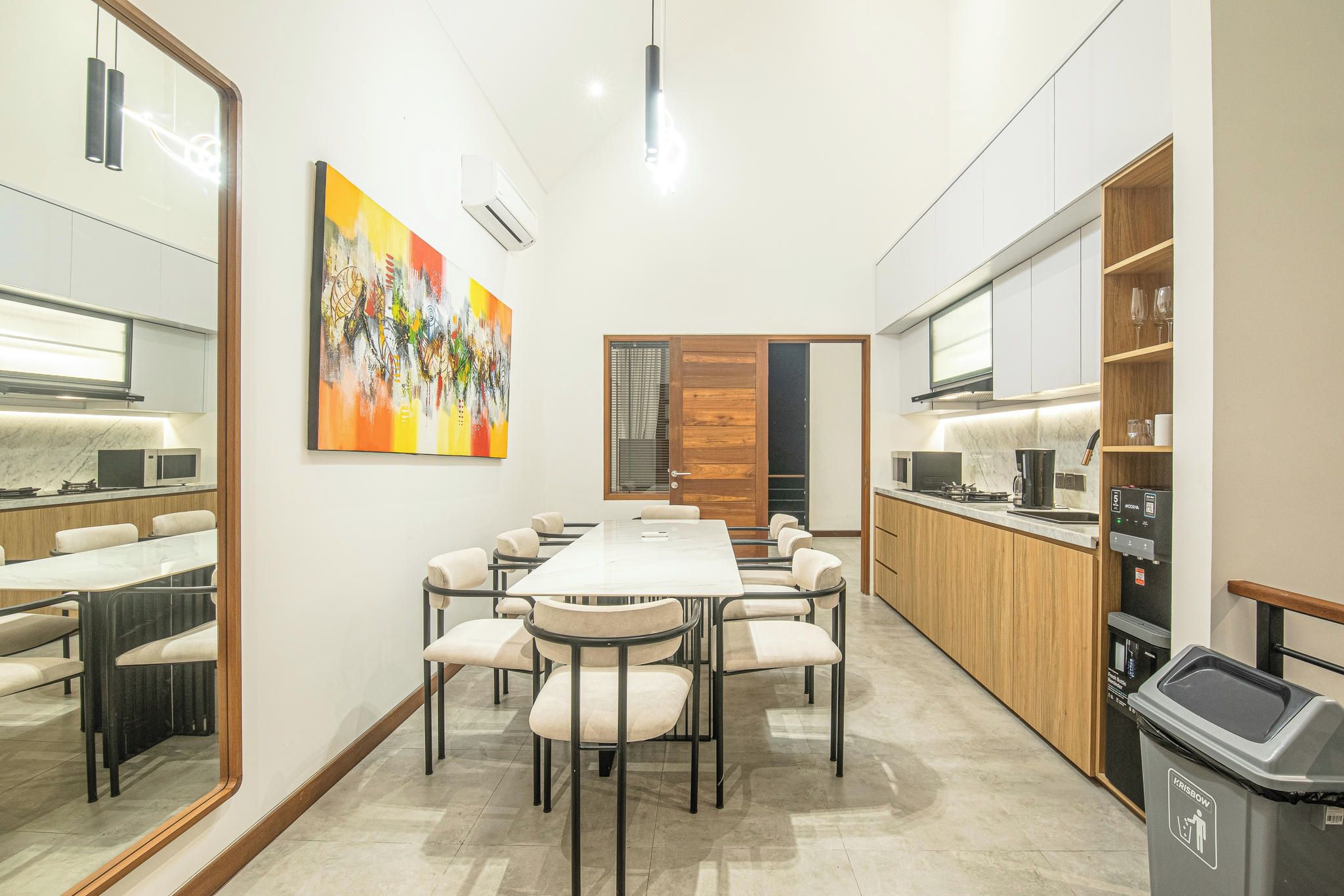 A modern kitchen with a dining area, a large painting on the wall, and a trash bin.