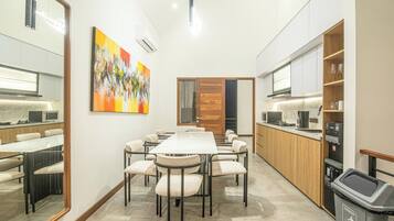 A modern kitchen with a dining area, a large painting on the wall, and a trash bin.
