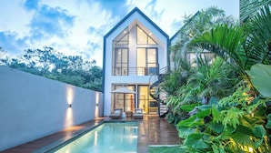 Una casa moderna con piscina, mobiliario exterior y abundante vegetación.