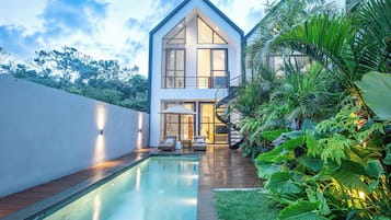 A modern house with a swimming pool, outdoor seating, and lush greenery.