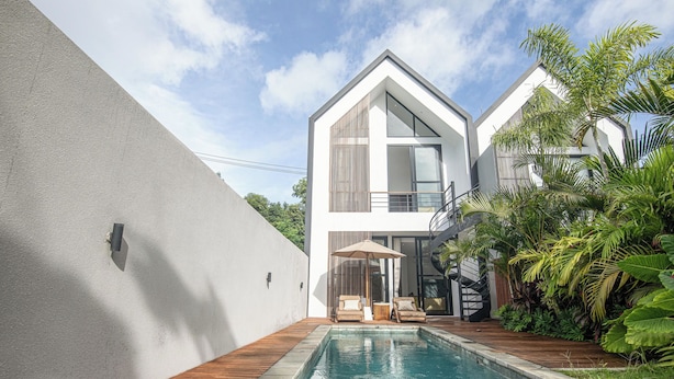 Una casa moderna de dos pisos con piscina, terraza de madera y plantas tropicales.